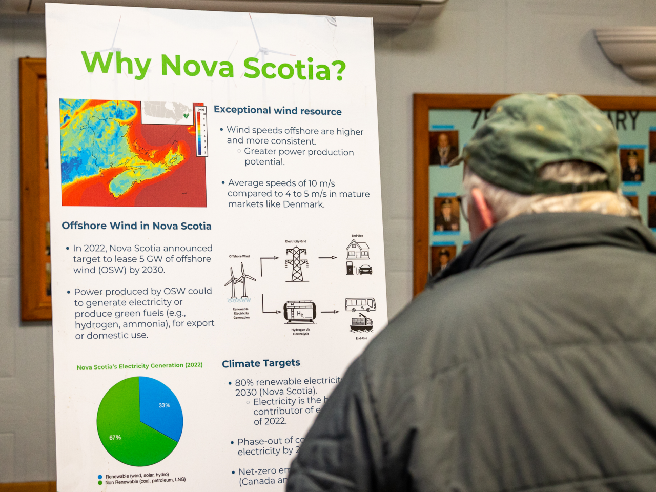 A community member reads an information board titled "Why Nova Scotia?"